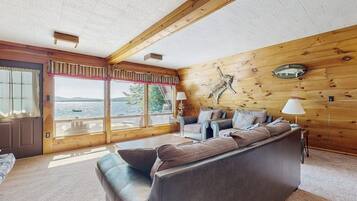 A cabin interior with a large window, wooden walls, a sofa, and a lamp.