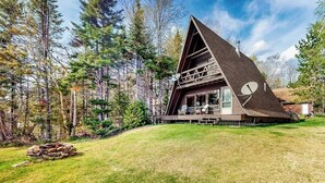 A wooden cabin with a triangular roof, surrounded by a forest. - Comfy Lakefront Cabin With Gorgeous Views, Private Dock & Pebble Beach (Greenville)