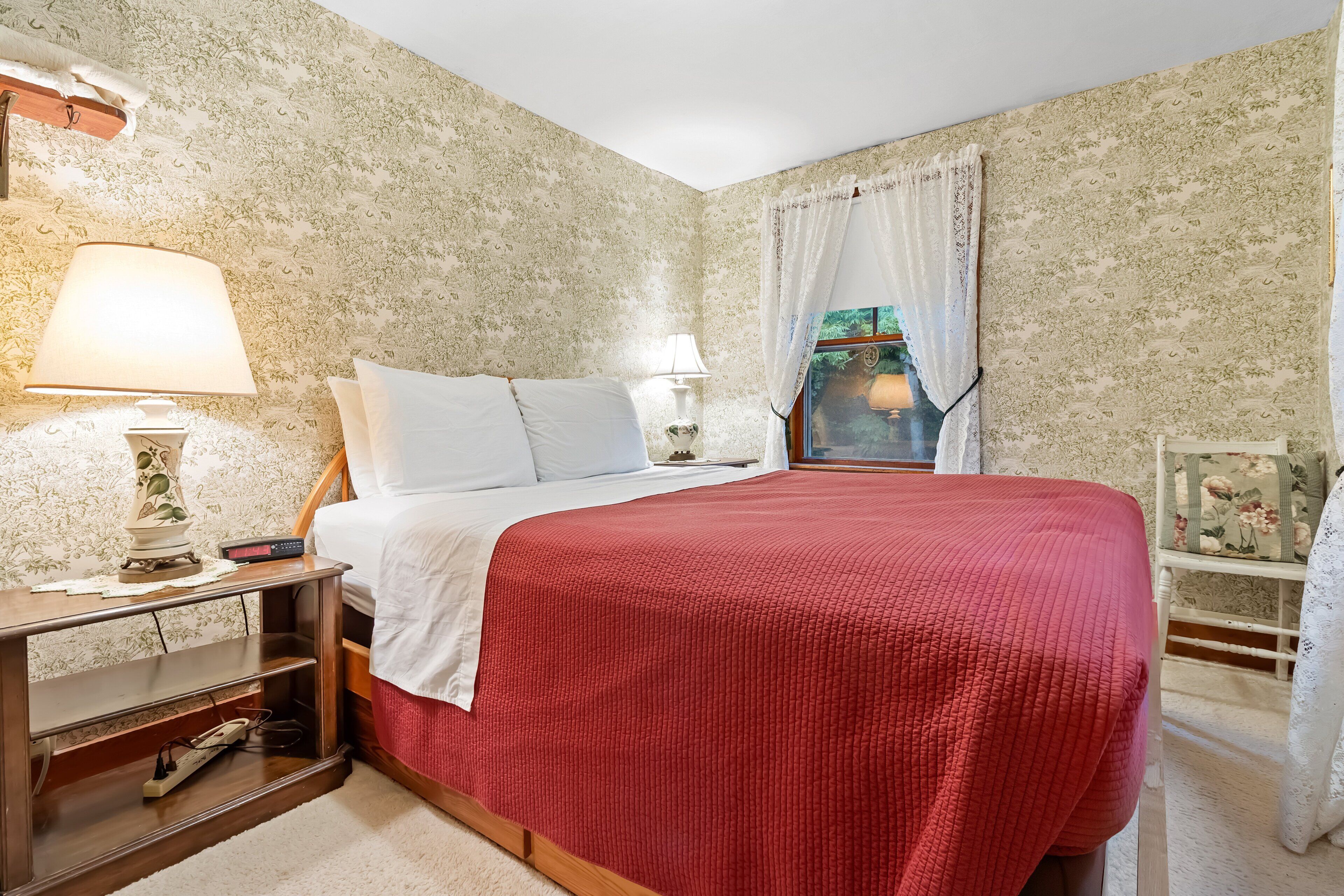 A bedroom with a bed, bedside lamps, a nightstand, and a window with curtains.