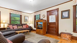 A living room with a sofa, armchairs, a coffee table, a television, and a wooden cabinet. - Century-old Oceanfront Home With Wraparound Porch - Walk Downtown, Dogs OK (Boothbay Harbor)