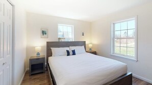 Un dormitorio con una cama, dos mesitas de noche y dos ventanas.