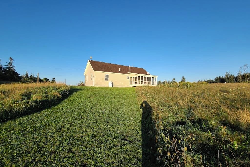 A large, single-story building with a sloped roof, situated on a grassy hill with a clear sky.