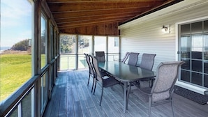 Un espacio comedor al aire libre techado, con una mesa y sillas, ventanas amplias y vistas del exterior.