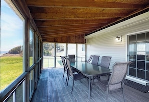 A covered outdoor dining area with a table and chairs, large windows, and a view of the outdoors. - Tranquil Getaway on the Coast With Beach Access, Ocean Views, & Screened Porch (Tenants Harbor)