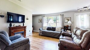 A living room with a fireplace, a television, a sofa, and a leather couch. - Charming Cottage Near the Beach With Balcony, Deck, Grill, Fireplace - Dogs OK (Georgetown)