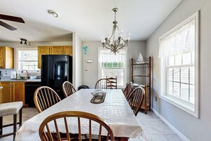 Uma cozinha com mesa de jantar, cadeiras, um lustre e uma geladeira.