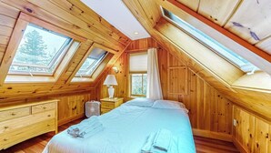 Ett sovrum med ett sluttande tak, takfönster, en säng, ett sängbord, en lampa och ett fönster.