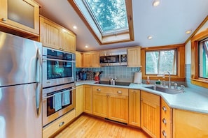 A modern kitchen with wooden cabinets, stainless steel appliances, a skylight, and a large window. - Well-equipped Cottage With Modern Touches, Wifi, gas Grill, & Beautiful Views (Port Clyde)