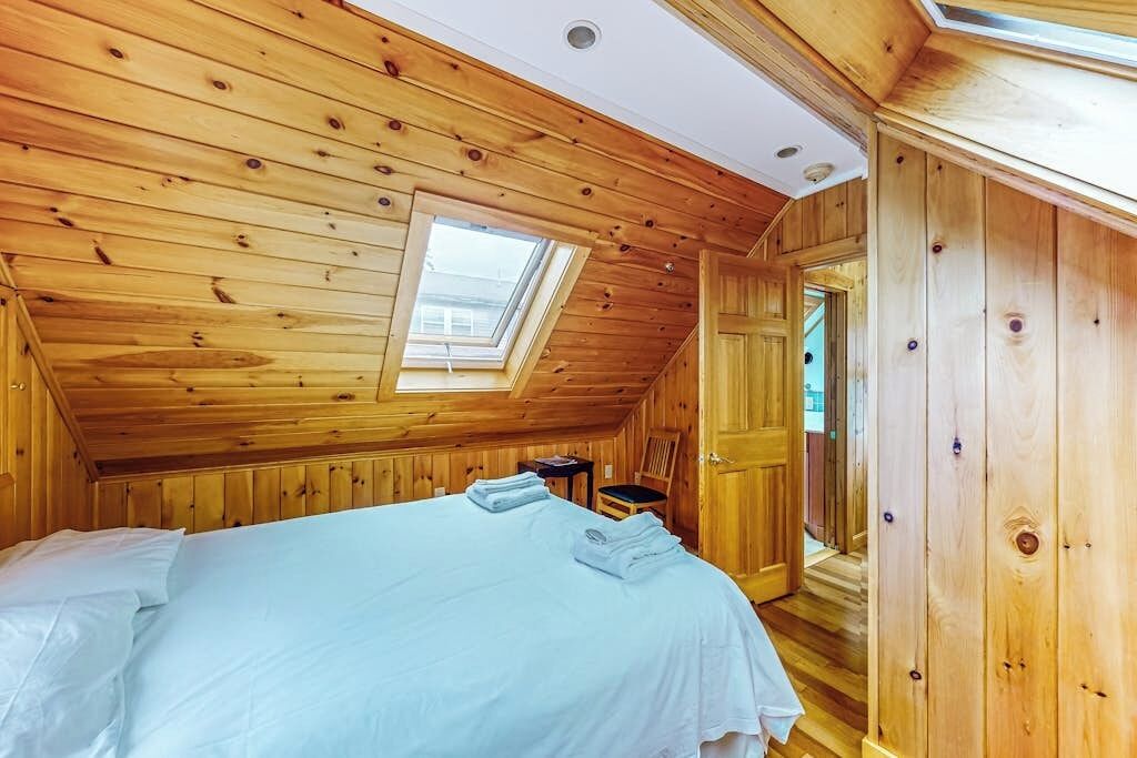 A wooden room with a bed, a skylight, and a door.