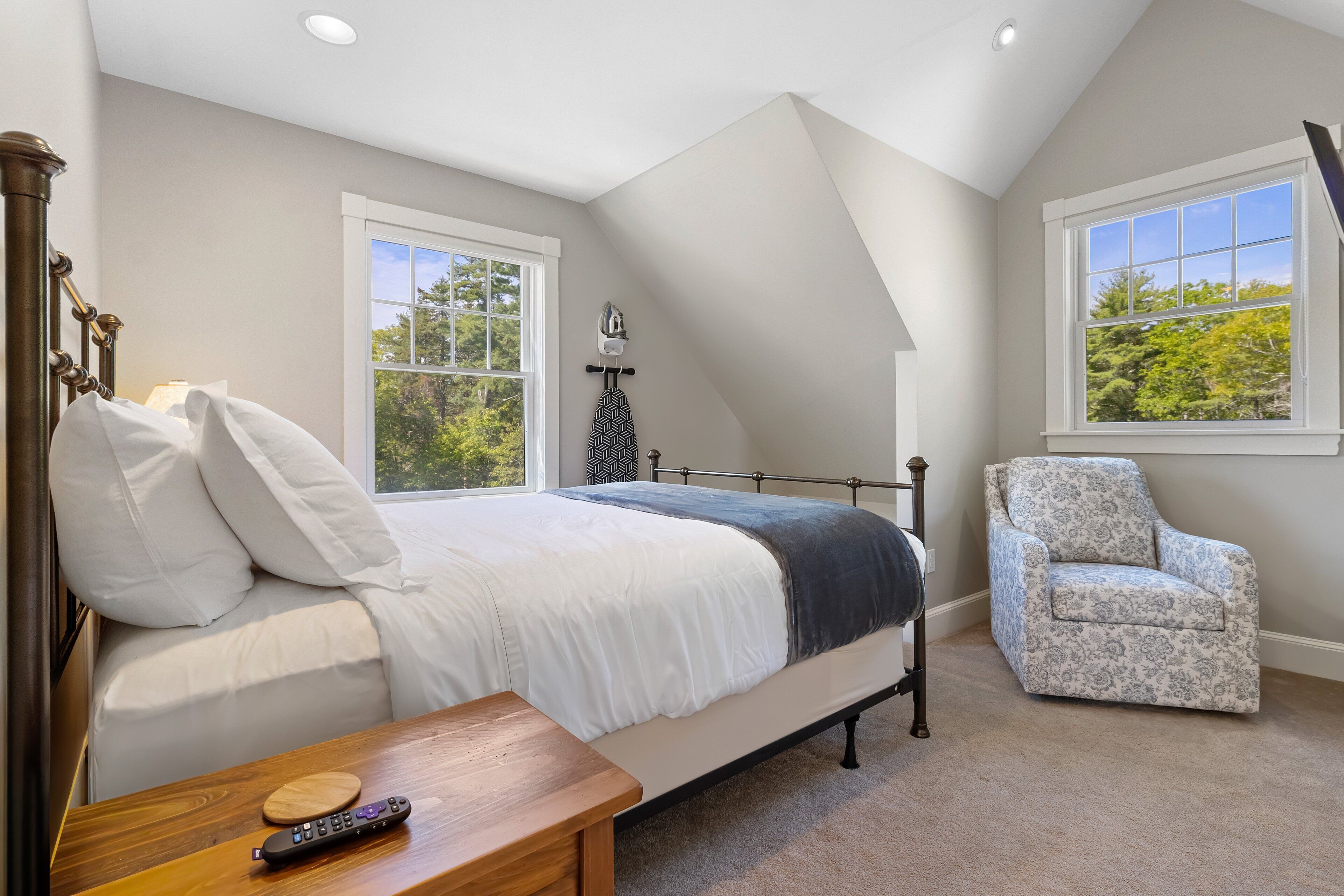 A bedroom with a bed, a chair, a nightstand, a lamp, and a window with a view of trees.