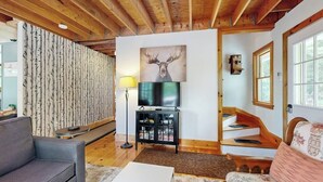 Ett vardagsrum med en soffa, ett soffbord, en tv på ett tv-bord, en lampa och en trappa.
