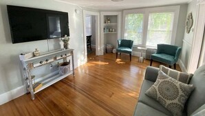 A living room with a TV, sofa, and teal chairs. - Historic Condo in Downtown Camden, Steps to Harbor (Camden)