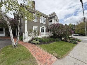 A two-story house with a brick pathway leading to the front door, surrounded by well-maintained grass and shrubs. - Historic Condo in Downtown Camden, Steps to Harbor (Camden)