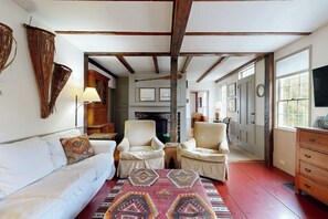 Ein gemütliches Wohnzimmer mit einem weißen Sofa, zwei Sesseln, einem gemusterten Teppich und einem Kamin.