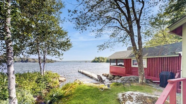 A lakeside cabin with a dock, a grassy area, and a red building.