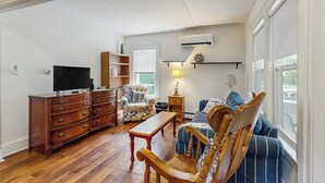 Una sala de estar con un aparador de madera, un televisor, un sillón estampado, un sofá azul y una lámpara.