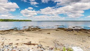 Ein Strand mit Kieselsteinen und Felsen, einem klaren Himmel und ruhigem Wasser.