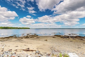 A beach with pebbles and rocks, a clear sky, and a calm body of water. - Cozy Studio With Lofted Sleeping Space and Great Water View (Surry)