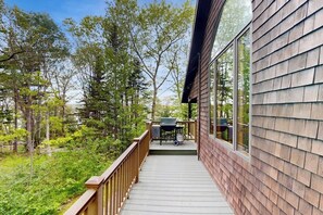 Eine Holzterrasse mit Grill und Gartenmöbeln, umgeben von Bäumen.