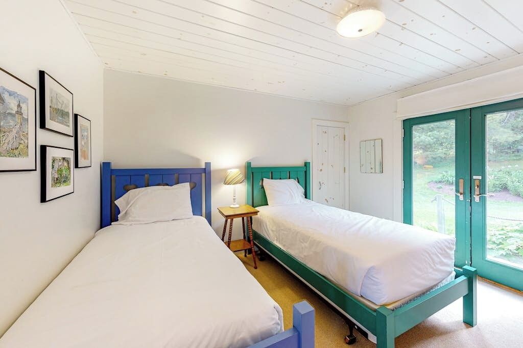 A bedroom with two single beds, a small bedside table with a lamp, and a door leading to a garden.