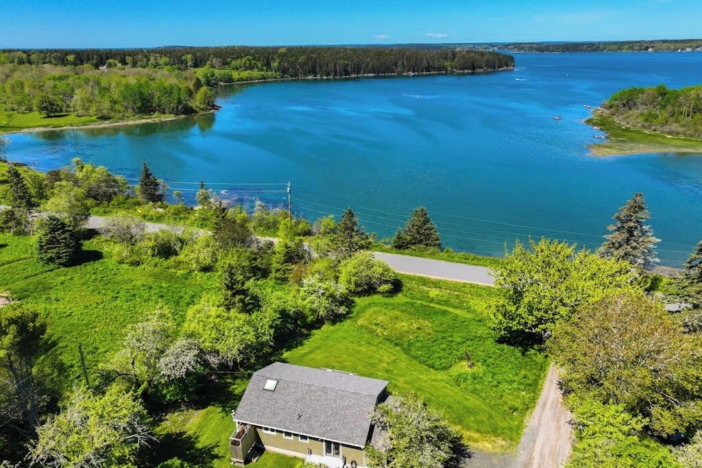 A house with a sloped roof, surrounded by a well-maintained lawn and a large body of water.
