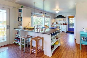 A kitchen with a central island, bar stools, a sink, and a window. - Dog-friendly Bayfront Home Close to Rockland With Water View - Snowbirds Welcome (Tenants Harbor)