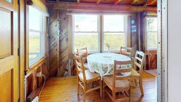A wooden dining room with a round table and six chairs, large windows, and a view of the outdoors.