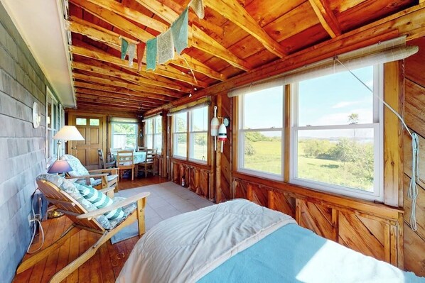 A wooden cabin with a bed, a chair, a table, and large windows.