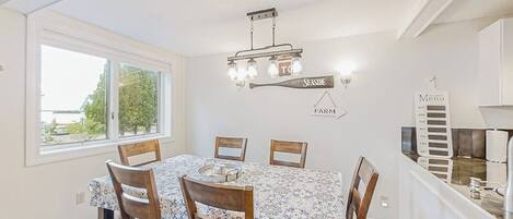 Un espace repas comprenant une table, des chaises, un lustre, une fenêtre et un comptoir de cuisine.