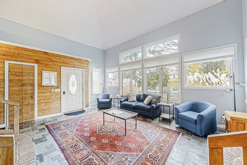 Un salon spacieux avec une grande fenêtre, un canapé bleu, une table basse et un tapis à motifs.