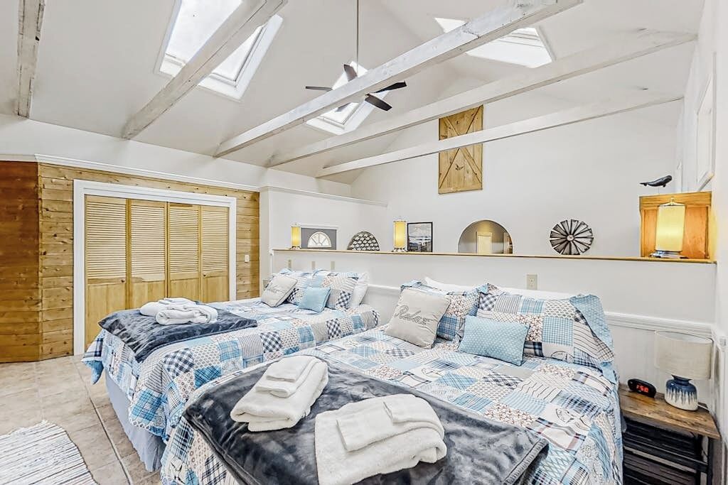 A bedroom with two beds, a skylight, wooden walls, and a small shelf with decorative items.