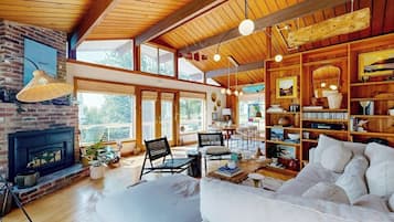 A spacious living room with a fireplace, wooden ceiling, and large windows.