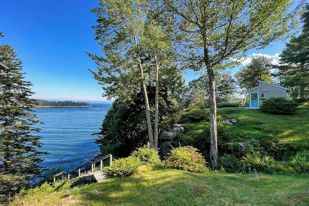 A coastal property with a wooden deck, a small building with a blue door, and a view of the sea.