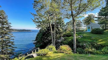 A coastal property with a wooden deck, a small building with a blue door, and a view of the sea.