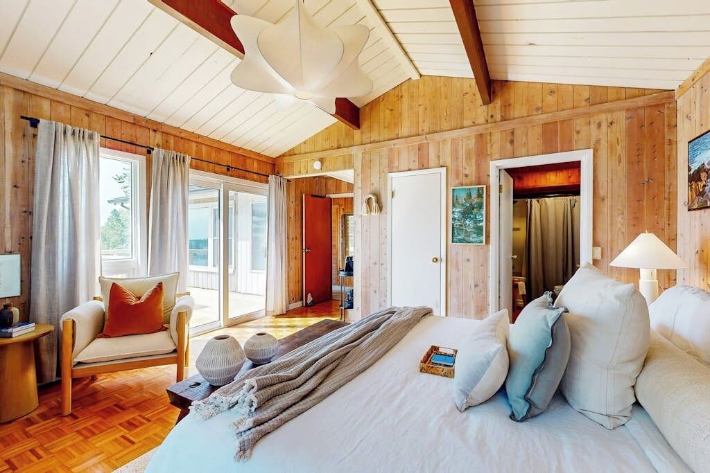A wooden-paneled room with a bed, a chair, and a table.
