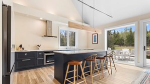 Uma cozinha moderna com uma ilha central, banquetas e vista para o exterior.