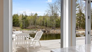 Um deck de madeira com uma cadeira e mesa, com vista para um lago e floresta.
