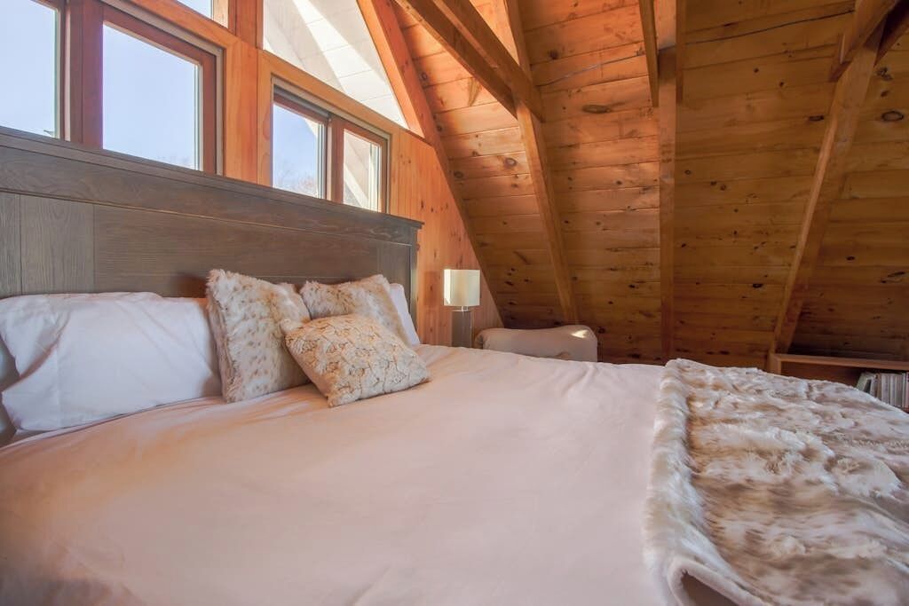 A bedroom with a wooden ceiling, a bed with white bedding, and a window.