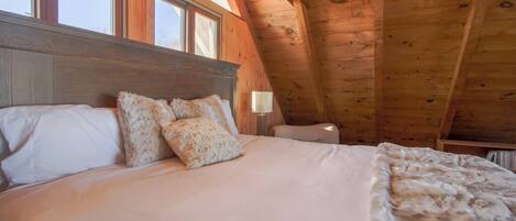 A bedroom with a wooden ceiling, a bed with white bedding, and a window.