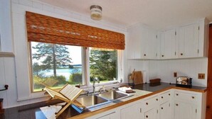 A kitchen with white cabinets, a wooden countertop, a window with a view of trees and a body of water, and a built-in sink. - Tideriver, Waterfront Cottage in Maine (Port Clyde)