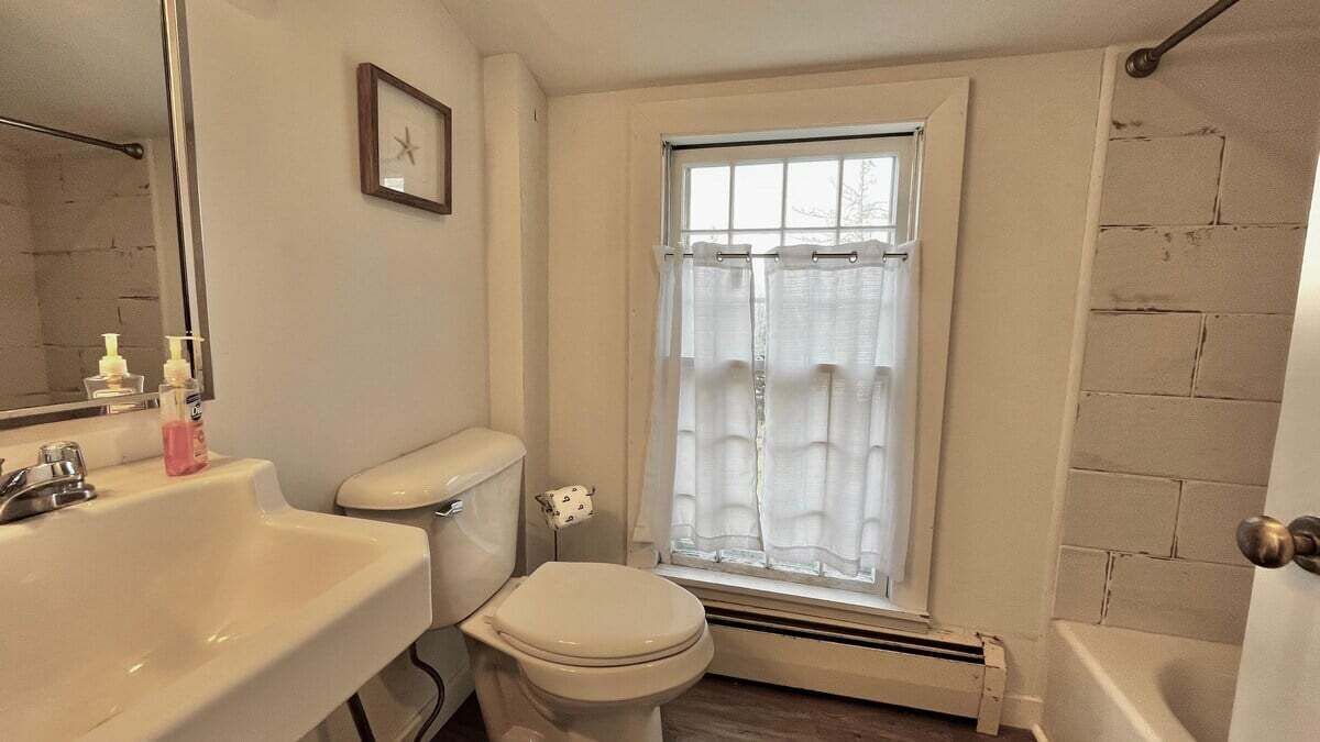 A bathroom with a sink, toilet, and window with curtains.
