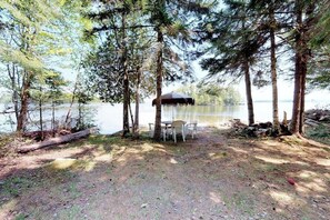Een kampeerterrein aan het meer, met een tafel en stoelen, omringd door bomen.