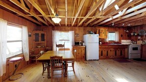 Ein Holzhäuschen im Inneren mit Esstisch, Stühlen, einer Küchenzeile mit Geräten und einem Fenster.