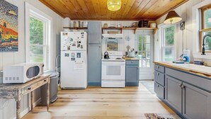A kitchen with wooden ceiling, white appliances, and a rustic table. - Charming Oceanfront Home With Stunning Water Views and Wifi (Georgetown)