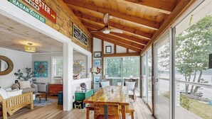 A spacious room with a large wooden dining table, a ceiling fan, and large windows offering a view of the outdoors. - Charming Oceanfront Home With Stunning Water Views and Wifi (Georgetown)