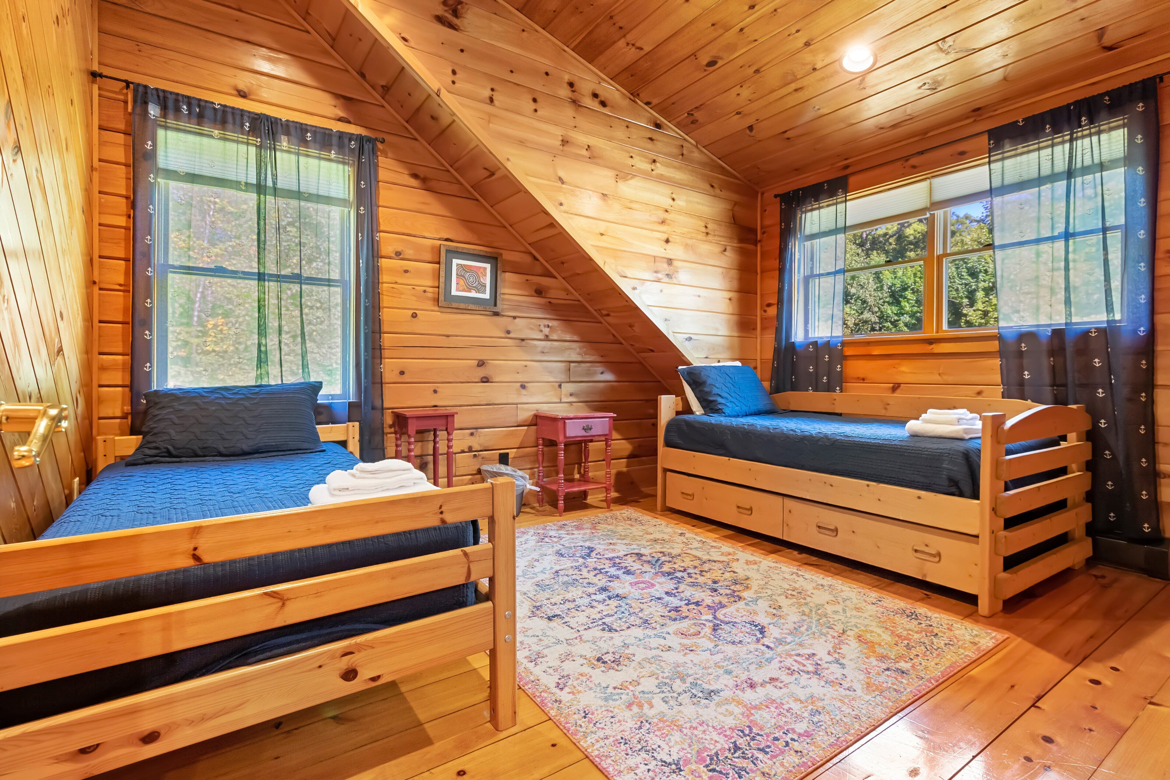 A cabin with two wooden beds, a small rug, and a picture on the wall.