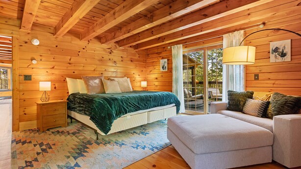 Interno di una baita di legno con un letto, un divano e vista all'aperto attraverso una porta vetrata.