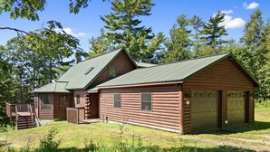 Una baita in legno con tetto in lamiera verde, un patio in legno e un garage.