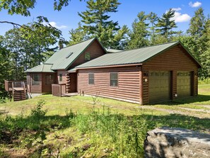Eine Blockhütte mit einem grünen Metall-Dach, einer Holzterrasse und einer Garage.