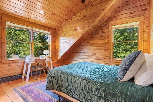 Un dormitorio de cabaña de madera con una cama, un escritorio y una silla.